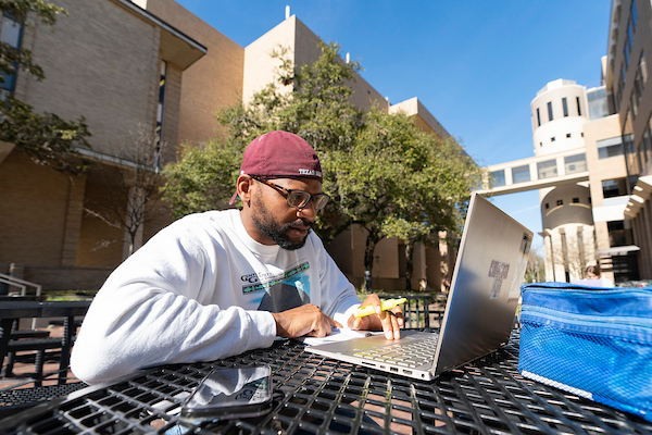 Student sitting outside at a table studying on his computer