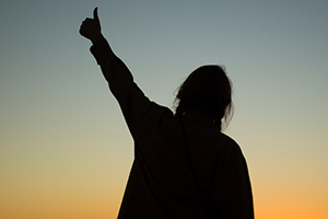 silhouette of a female presenting student gesturing with a thumbs up during sunset