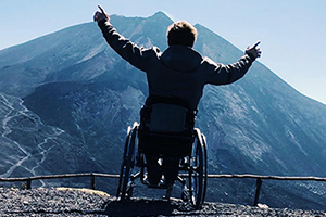 Image of student in wheel chair with airs raised in front of a mountain range