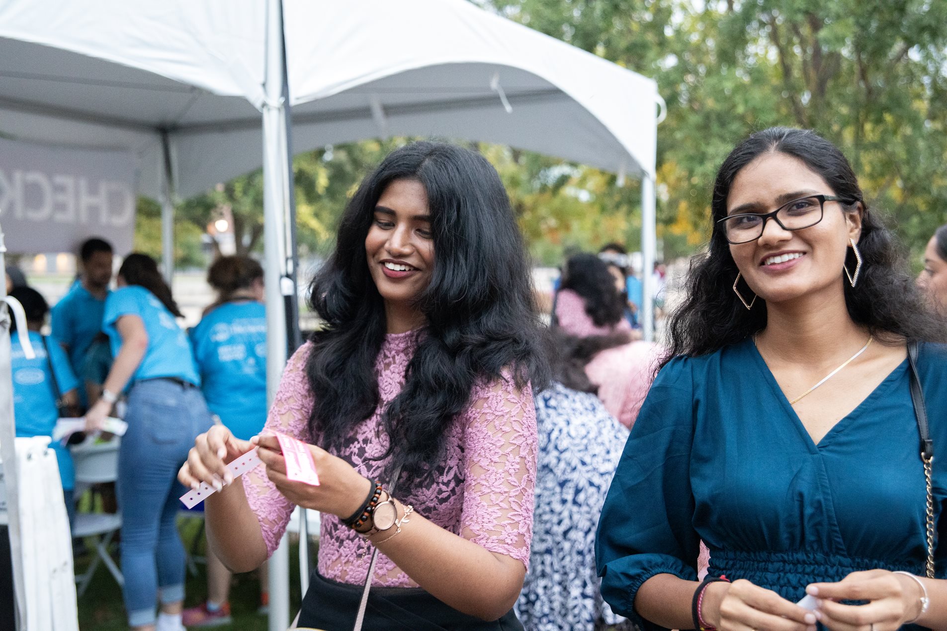 Two individuals smiling and holding tickets at the 2024 Texas A&M Global Welcome Party with a tent labeled "CHECK-IN" in the background.